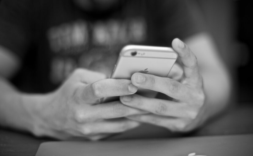 A black and white photo of a man holding a smartphone with two hands and the Apple logo is just visible on the back