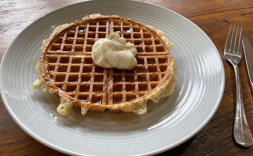 Shows a waffle covered with syrup and a dollop of yoghurt sprinkled with cinnamon