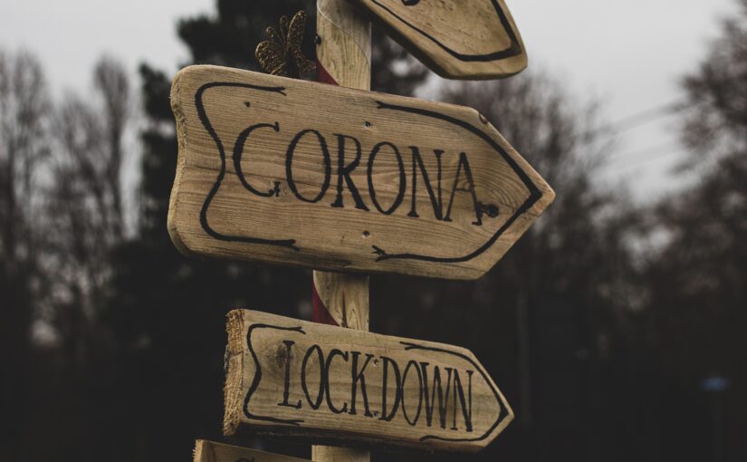 A wooden sign with words attached saying CORONA and LOCKDOWN