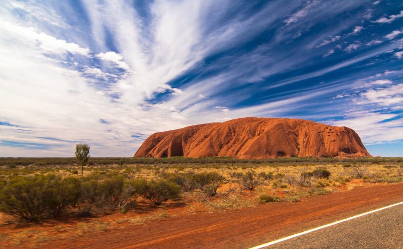 Photograph of Uluru in the day with a blue sky and white clouds